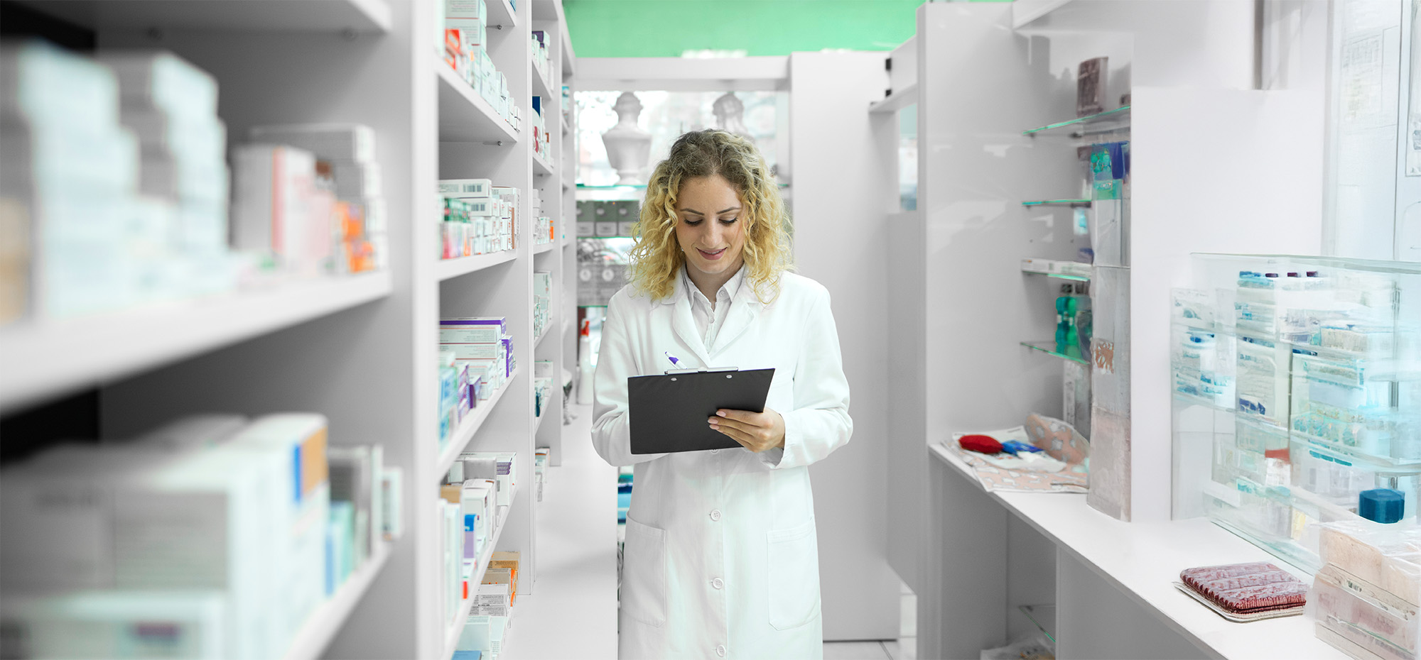 Pharmacist in white uniform walking by the shelf with medicines and checking inventory